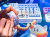 Implant dentaire : maquette de prothèse sur implants tenue devant un plateau d'instruments chirurgicaux