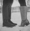 Jambes d'un couple face à face dans la neige, en noir et blanc, la femme sur la pointe des pieds