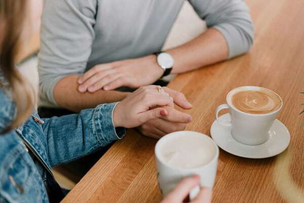 Mains d'un couple qui se rejoignent sur une table autour d'un café