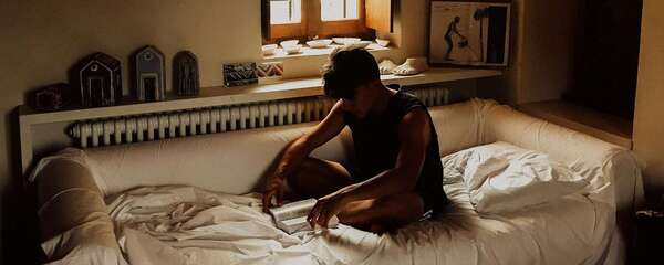 Un homme assis au bord du lit dans la lumière du matin, illustrant l'anxiété de performance sexuelle quand le désir est là mais que le corps bloque