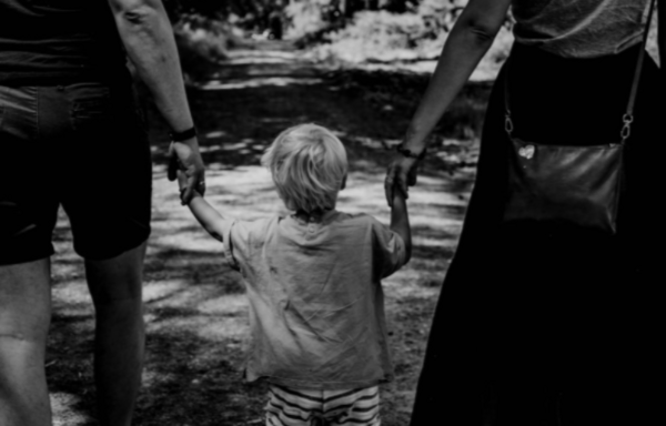 Un enfant avec son sac à dos entre ses deux parents dans la lumière du matin, illustrant la coparentalité après une séparation
