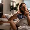 jeune femme qui semble anxieuse et en réflexion à côté de son mari qui dort