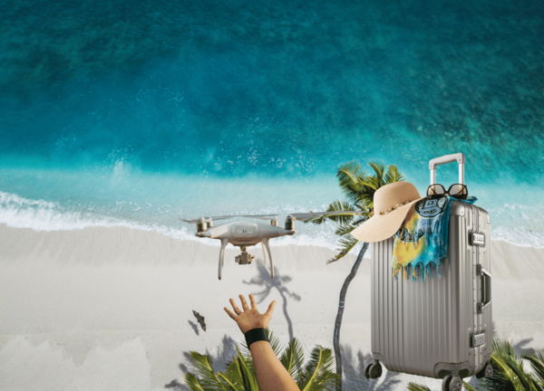 Un drone s’envole au-dessus d’une plage paradisiaque, valise à la main : l’illustration idéale pour parler de voyage, de réglementation drone à l’étranger et de conseils pour voler sereinement en vacances.