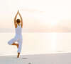 Femme en posture de yoga sur plage calme au coucher de soleil