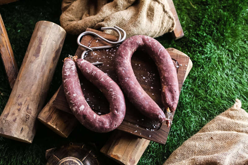 vue-de-dessus-saucisse-fumee-sur-un-plateau-avec-du-bois-de-chauffage-et-des-sacs-de-jute-sur-l-herbe