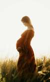 Femme enceinte debout en robe rouille dans un champ lumineux
