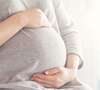 Femme enceinte en robe grise tenant son ventre arrondi
