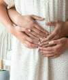 Femme enceinte en robe blanche entourée tendrement par son partenaire