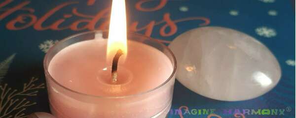 Une bougie rose parfumée à la rose éclaire 2 belles pierres de lithothérapie : un quartz rose et une agate rose marbrée. Le tout est posé sur les mots rose Happy holidays.