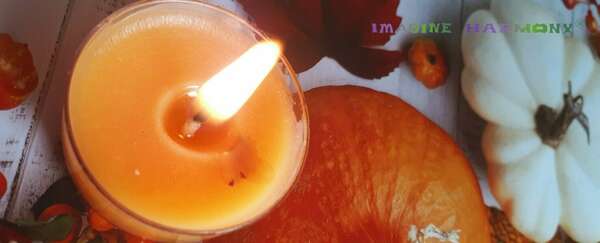 Une bougie orange scintille à côté d'une pastèque, d'un pâtisson blanc, de petits fruits rouges et de feuilles d'automne.