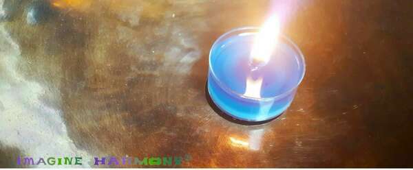 Une bougie bleu parfumée à l'huile essentielle de tanaisie est posée au fond d'un grand bol tibétain. La flamme de la bougie éclaire l'alliage des 7 métaux du bol tibétain.