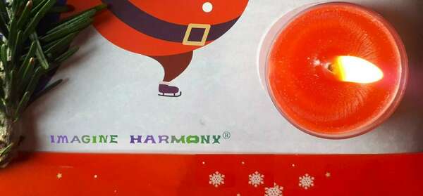 Une bougie rouge parfumée à l'huile essentielle de camomille est allumée. Elle repose sur de la glace, une branche de sapin et des étoiles blanches sur fond rouge. Un père Noël patinant complète ce beau tableau. 