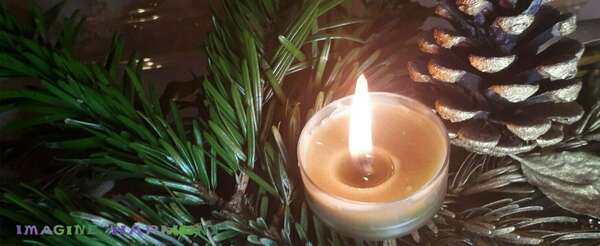 Une bougie à la cire d'abeille, couleur olive, est allumée avec un parfum de tanaisie. Elle repose sur des branches de sapin fraiches et d'autres branches séchées et dorés, accompagnée d'une pomme de pain dorée.