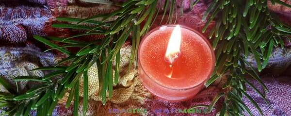 Une bougie orangée aux senteurs de camomille est allumée. Elle repose à côté d'une branche de sapin et sur un tissu orangé, rose, jaune rouge très doux.