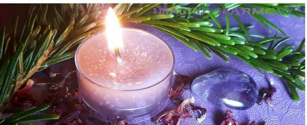 Une bougie mauve parfumée à la tanaisie est allumée. Elle repose à côté d'une améthyste, de branche de sapin, et de fleurs séchées de sauge arbustive.