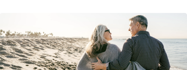 A smiling retired couple on a beach, illustrating real estate financing in France for expatriate retirees