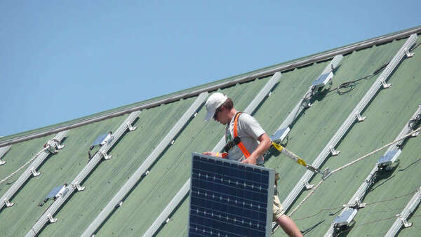 Couvreur installant un panneau solaire sur une toiture : une activité qui doit figurer au contrat décennale (photo USDA, domaine public)