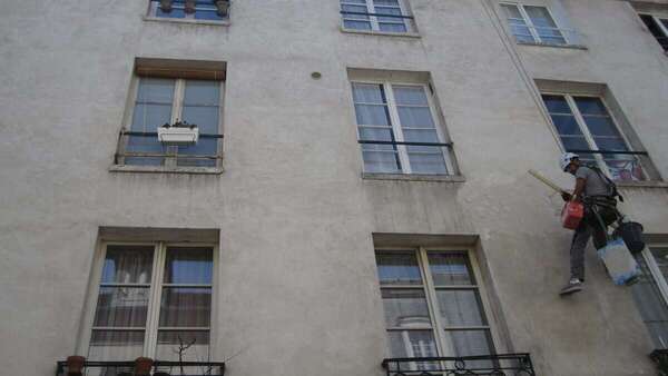 Mention garantie décennale sur les devis et factures : peintre en bâtiment au travail sur une façade d'immeuble à Paris