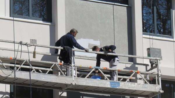 Facturation électronique pour un artisan du bâtiment : deux peintres en bâtiment au travail sur une nacelle, en façade d'un immeuble à Lyon