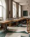 Salle de restaurant au sol revêtu de dalles en terrazzo beige ou vert aux formes graphiques enchevêtrées.  Mobilier bois dans les teintes de noyer, une essence chaleureuse