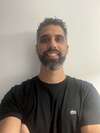 Chiropracteur souriant en pull bleu marine devant mur gris