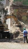 homme casque vert face pelleteuse jaune démolition bâtiment