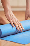 Personne en train de rouler un tapis de yoga bleu dans un espace lumineux pour un accompagnement bien-être