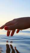 Main féminine avec vernis rouge touchant eau ondulante douceur EFT