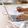Personne travaillant sur ordinateur portable avec documents et crayon