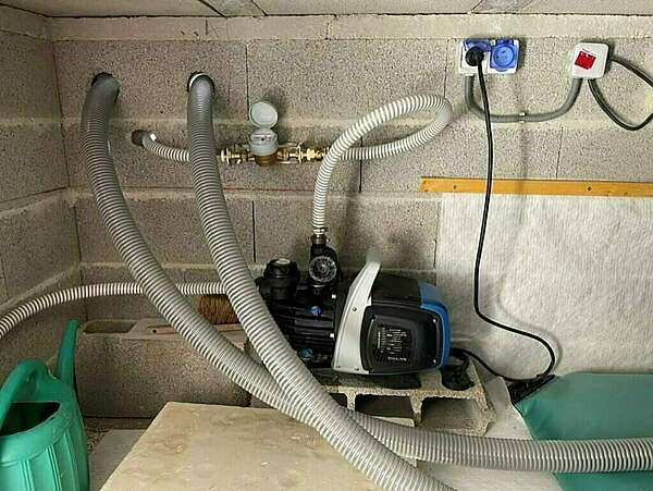 Raccordement d'une pompe à une citerne souple dans un vide sanitaire, installation avec tuyaux flexibles et système de raccordement électrique.