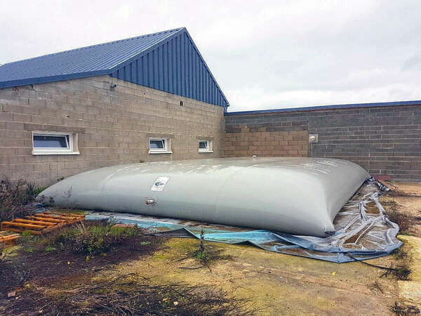 Citerne souple Citerpack de 99m3 installée à l'extérieur d'un bâtiment pour le stockage d'engrais liquide. Conçue pour les exploitations agricoles, cette citerne permet un stockage sécurisé et efficace des engrais liquides en grande quantité.