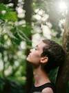 Une femme adossée contre un arbre, qui ferme les yeux et se repose en pleine nature