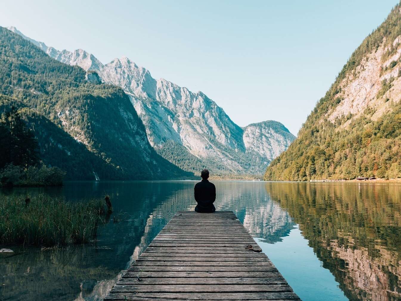 Un homme assis sur un ponton qui regarde un paysage au loin