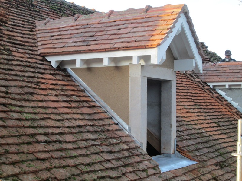 Lucarne à chevalet peinte en blanc avec poteaux en pierre jaune, jouée en enduit et vieille tuile plate.