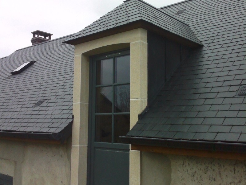 Lucarne capucine en ardoise avec poteaux en pierre blanche, corniche en chêne et jouée en zinc anthracite.