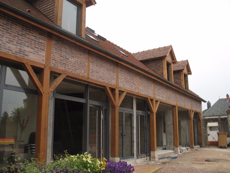 Charpente sur poteaux lasurée avec pans de bois et lucarnes.