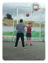Audrée, en tenue de sport, lance un ballon de basket à Pierre, face à elle. On voit un panier de basket au-dessus d'elle.