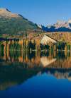 Lac de montagne clair entouré de forêt aux couleurs automnales avec une maison en bois à trois étages symbolisant la quête de sens